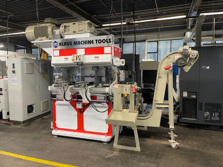 Industrielle Maschine von Klaus Machine Tools in einer Fabrikhalle, umgeben von weiteren Geräten, mit Förderband.