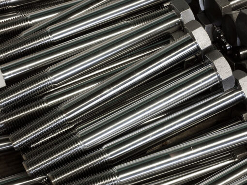 sonderschrauben-spezialschrauben-01-warmformteile-schmiedeteile-01 Stapel von Metallbolzen mit Muttern, glänzend und rostfrei, ideal für industrielle Anwendungen in der Maschinenbauindustrie.
